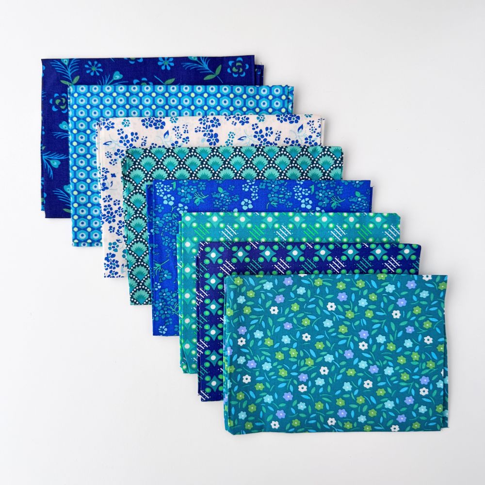 A folded set of Petit Pan Fabrics cotton fabric coupons in a blue floral pattern, wrapped in a white paper band with red text. Hanko Ivory Petit Pan Fabric Bundle | 8-Piece Coupon Kit